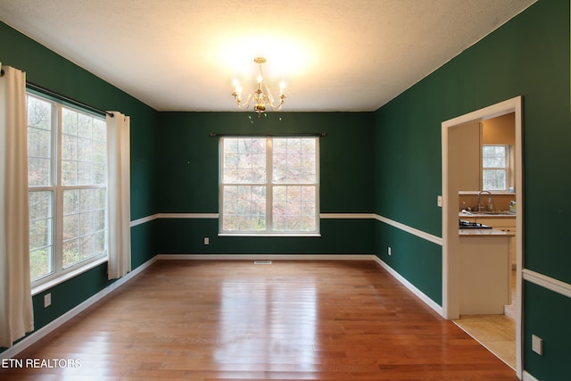 unfurnished dining area featuring sink, a chandelier, and light hardwood / wood-style floors