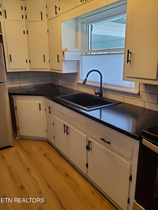 kitchen with light wood-type flooring, white cabinetry, fridge, and sink