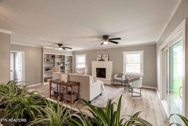 living room featuring ceiling fan, light wood-type flooring, ornamental molding, and a fireplace