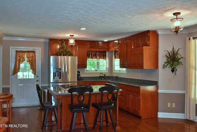 kitchen with stainless steel refrigerator with ice dispenser, a textured ceiling, ornamental molding, dark hardwood / wood-style floors, and a kitchen island