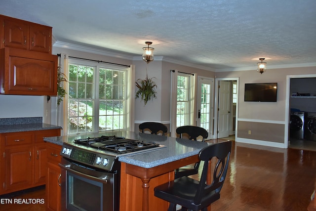 kitchen featuring crown molding, washing machine and dryer, stainless steel range with gas stovetop, a center island, and dark hardwood / wood-style flooring