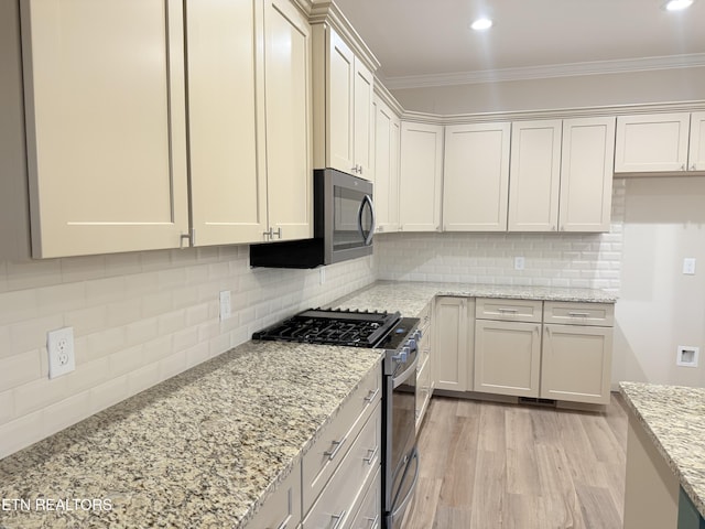 kitchen with light hardwood / wood-style floors, ornamental molding, tasteful backsplash, light stone counters, and appliances with stainless steel finishes