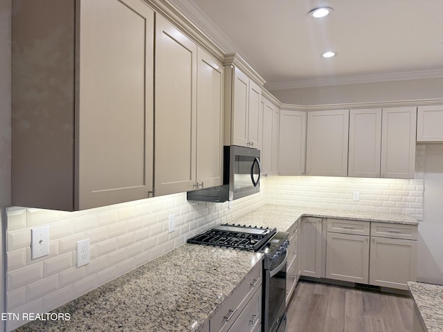 kitchen with light wood-type flooring, appliances with stainless steel finishes, light stone counters, and ornamental molding