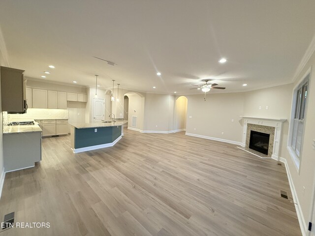 unfurnished living room featuring light hardwood / wood-style flooring, ceiling fan, ornamental molding, and sink