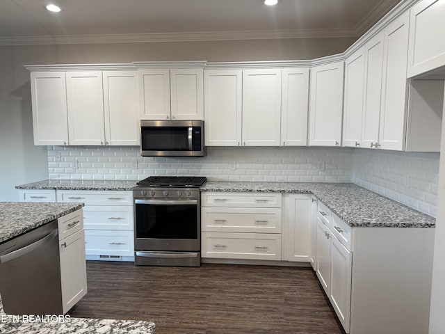 kitchen with light stone counters, stainless steel appliances, dark hardwood / wood-style flooring, white cabinets, and ornamental molding