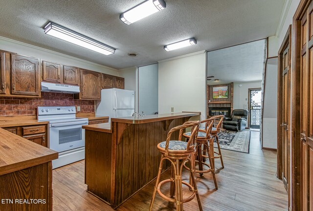 kitchen with a breakfast bar, white appliances, a brick fireplace, a textured ceiling, and tasteful backsplash