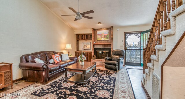 living room with a brick fireplace, light hardwood / wood-style flooring, ornamental molding, and lofted ceiling