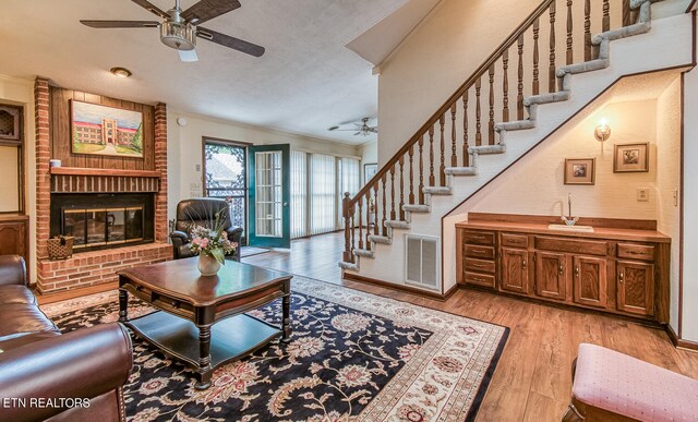 living room with ceiling fan, crown molding, light hardwood / wood-style floors, a textured ceiling, and a fireplace