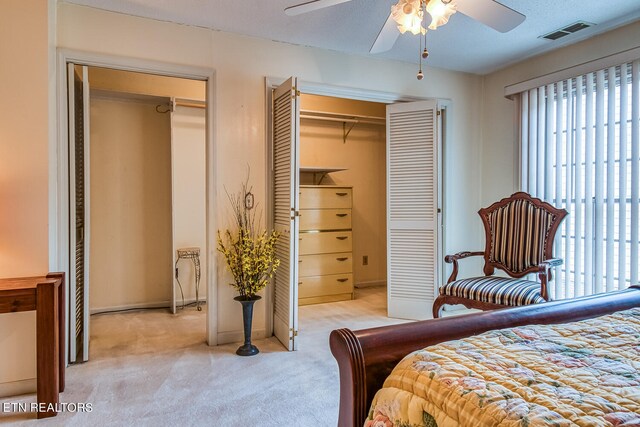 bedroom featuring light carpet, two closets, and ceiling fan