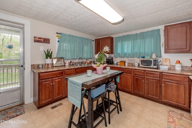 kitchen with a textured ceiling, sink, light tile floors, and light stone countertops