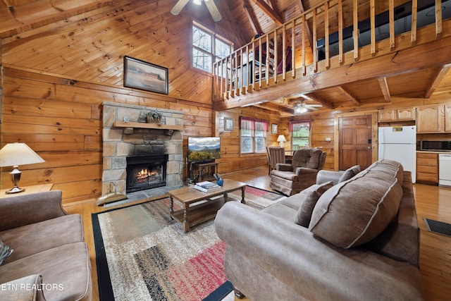 living room with wood walls, a healthy amount of sunlight, hardwood / wood-style flooring, a stone fireplace, and ceiling fan