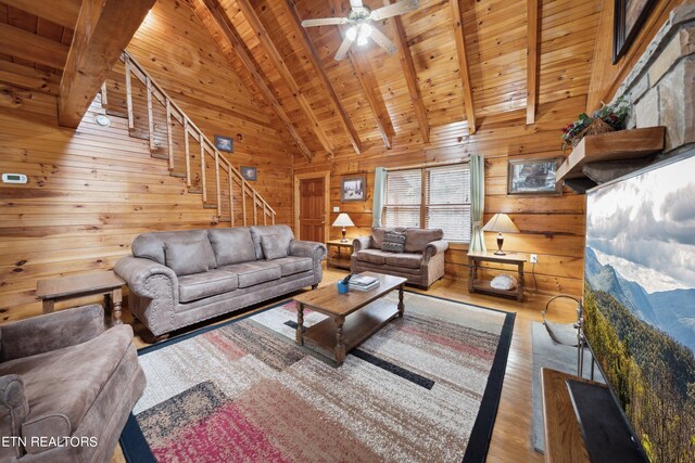 living room featuring wood walls, light hardwood / wood-style flooring, ceiling fan, beam ceiling, and wood ceiling