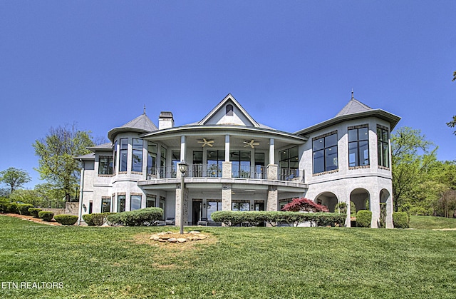 rear view of house featuring a lawn, ceiling fan, and a balcony