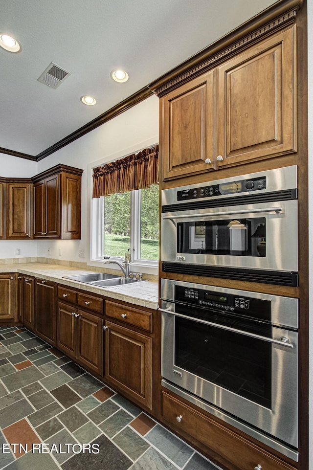 kitchen with stainless steel double oven, ornamental molding, and sink