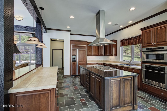 kitchen with island exhaust hood, stainless steel appliances, sink, pendant lighting, and a kitchen island