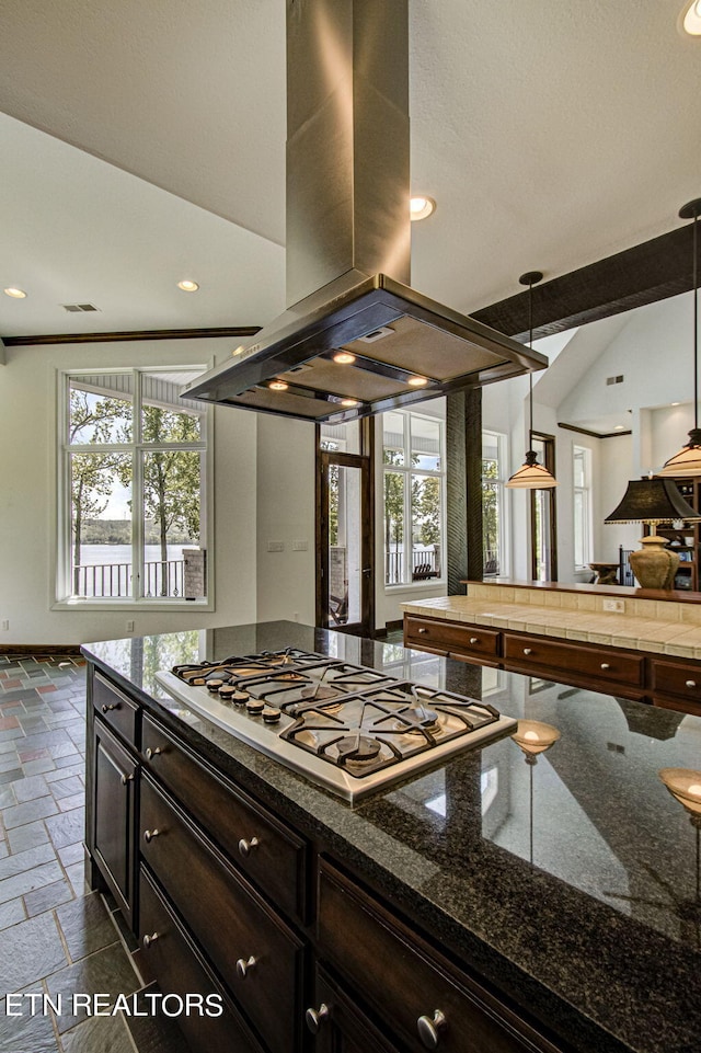 kitchen with dark brown cabinetry, island range hood, stainless steel gas cooktop, decorative light fixtures, and dark stone countertops