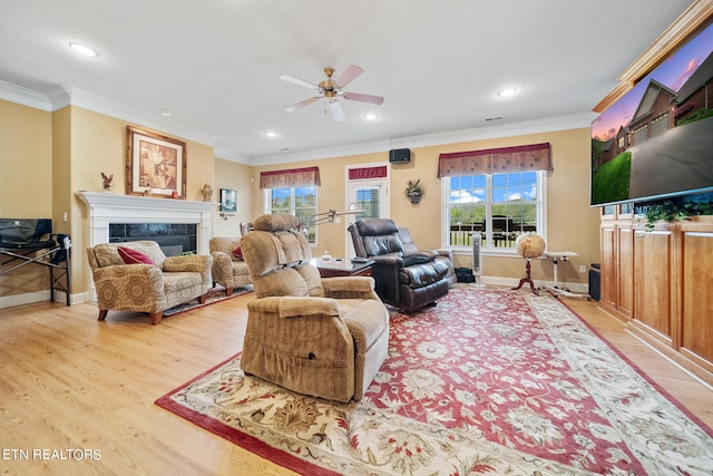 living room featuring crown molding, light hardwood / wood-style flooring, a tiled fireplace, plenty of natural light, and ceiling fan