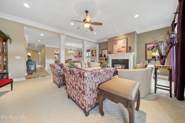 living room featuring light carpet, ceiling fan with notable chandelier, a tiled fireplace, crown molding, and ornate columns