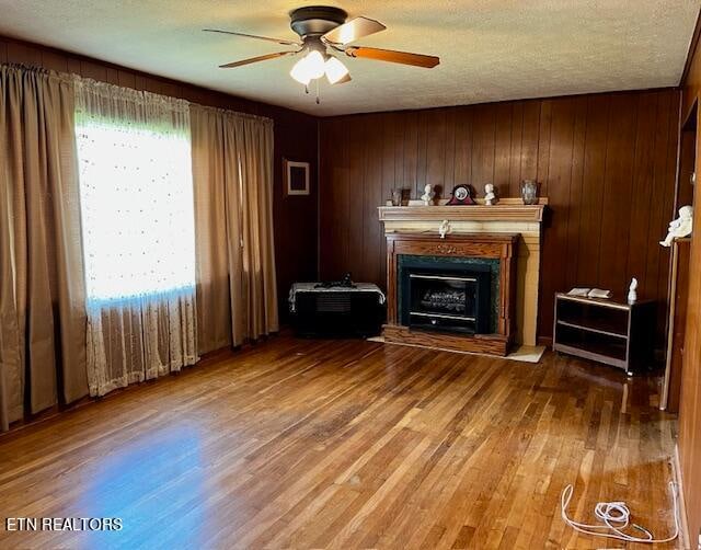 unfurnished living room with ceiling fan, wood walls, a textured ceiling, and hardwood / wood-style floors