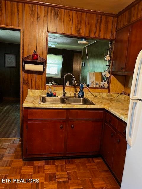 kitchen featuring wood walls, dark parquet flooring, sink, and white fridge