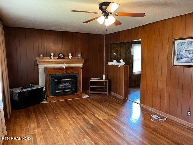 unfurnished living room featuring ceiling fan, wood walls, a textured ceiling, and hardwood / wood-style flooring