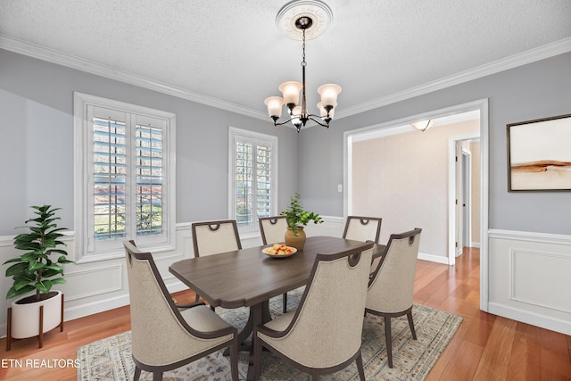 dining room with a textured ceiling, light hardwood / wood-style floors, an inviting chandelier, and ornamental molding