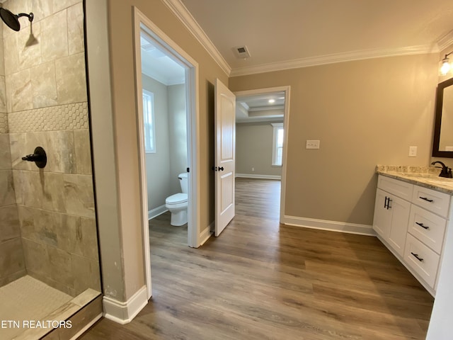 bathroom with toilet, vanity, ornamental molding, a tile shower, and hardwood / wood-style flooring