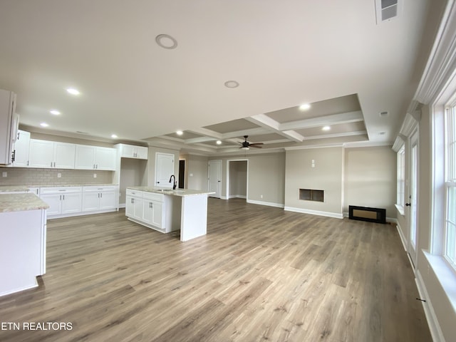 kitchen with coffered ceiling, a center island with sink, ceiling fan, beam ceiling, and white cabinetry