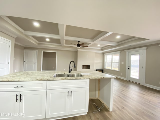 kitchen featuring light stone countertops, white cabinetry, ceiling fan, coffered ceiling, and sink