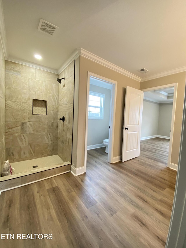 bathroom featuring toilet, a tile shower, crown molding, and wood-type flooring