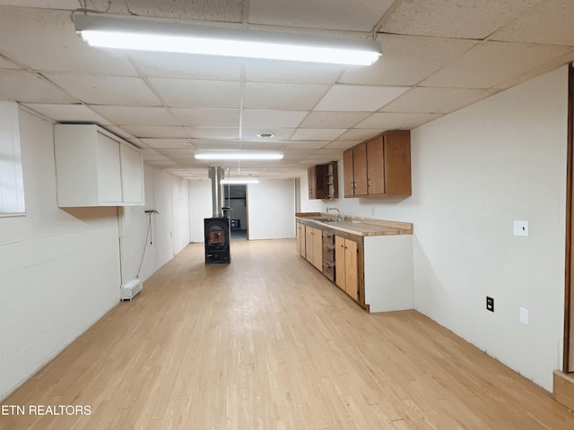 kitchen with light wood-type flooring, a wood stove, stainless steel dishwasher, and sink