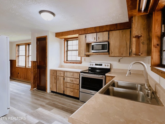 kitchen with sink, wood walls, light hardwood / wood-style floors, a textured ceiling, and appliances with stainless steel finishes