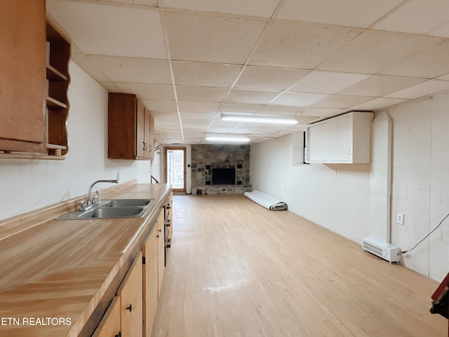 kitchen featuring a fireplace, sink, a drop ceiling, and light hardwood / wood-style floors