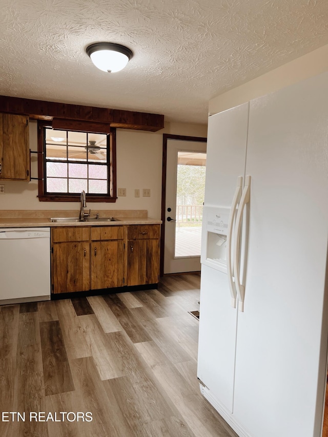 kitchen featuring a textured ceiling, a wealth of natural light, light hardwood / wood-style floors, and white appliances