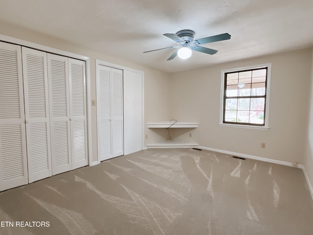 unfurnished bedroom featuring a textured ceiling, ceiling fan, carpet, and two closets