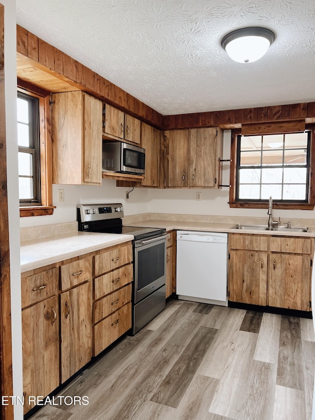 kitchen with a textured ceiling, light hardwood / wood-style floors, sink, and appliances with stainless steel finishes