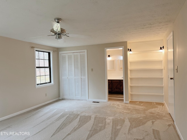 unfurnished bedroom with ceiling fan, a textured ceiling, connected bathroom, light colored carpet, and a closet