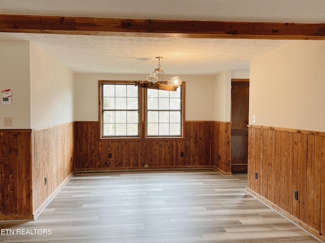 empty room featuring a notable chandelier, a textured ceiling, wooden walls, and light hardwood / wood-style flooring