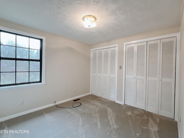 unfurnished bedroom with carpet, a textured ceiling, and two closets