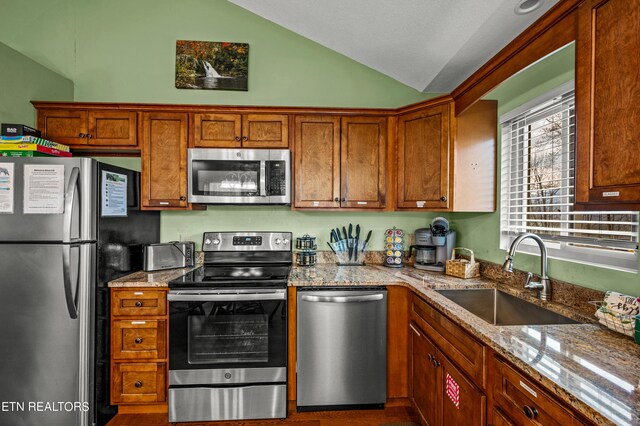 kitchen with lofted ceiling, sink, stainless steel appliances, and light stone counters