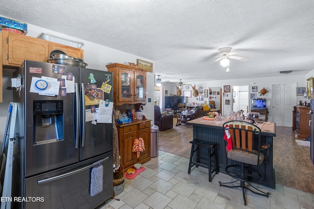 kitchen with a breakfast bar, ceiling fan, light tile floors, and stainless steel fridge