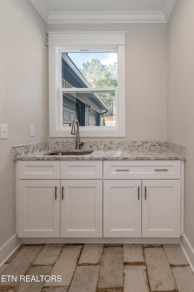 interior space featuring ornamental molding, sink, white cabinets, and light stone counters