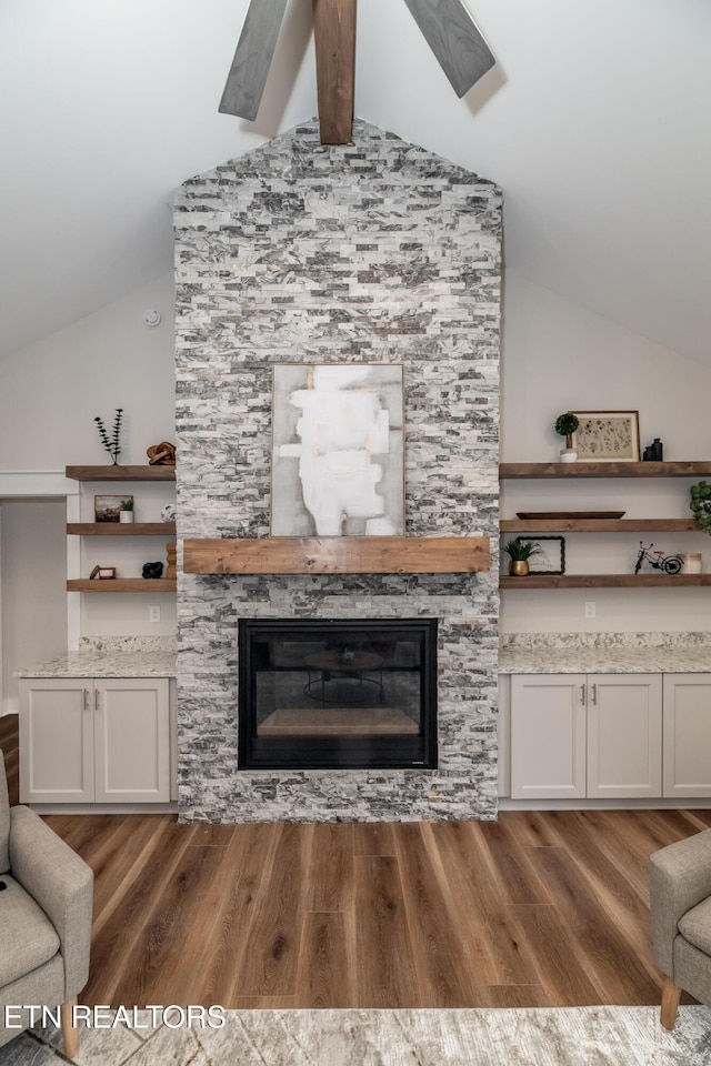 living room featuring a stone fireplace, hardwood / wood-style floors, and vaulted ceiling with beams