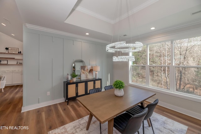 dining area featuring crown molding, an inviting chandelier, a raised ceiling, and hardwood / wood-style floors