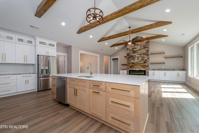 kitchen featuring sink, stainless steel appliances, an island with sink, backsplash, and a stone fireplace