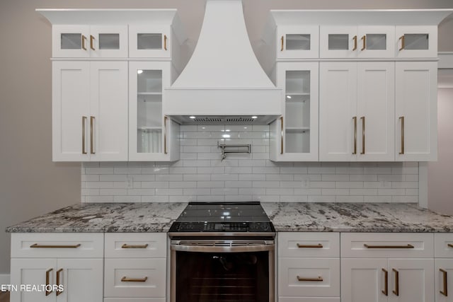 kitchen featuring white cabinets, stainless steel range with electric cooktop, custom range hood, and decorative backsplash