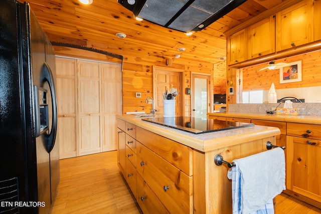 kitchen with wooden walls, a center island, light wood-type flooring, black refrigerator with ice dispenser, and wood ceiling