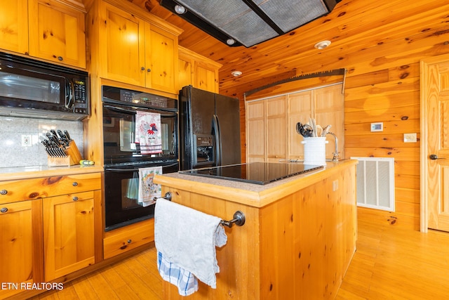 kitchen featuring light hardwood / wood-style flooring, a center island, backsplash, and black appliances