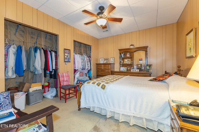 bedroom featuring wooden walls, ceiling fan, a closet, and a paneled ceiling