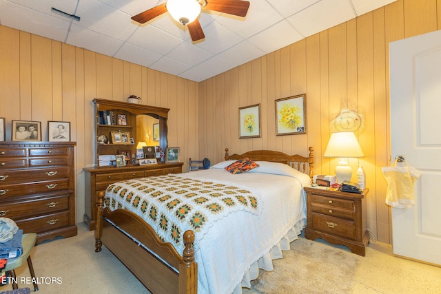 bedroom featuring ceiling fan, a paneled ceiling, and wood walls